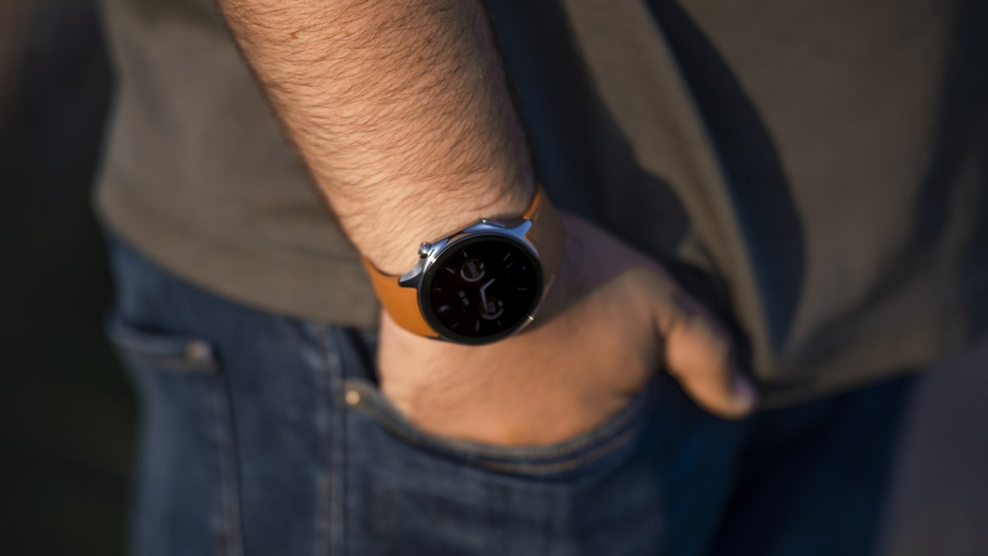 OPPO Watch X dans une main d'homme devant des vêtements