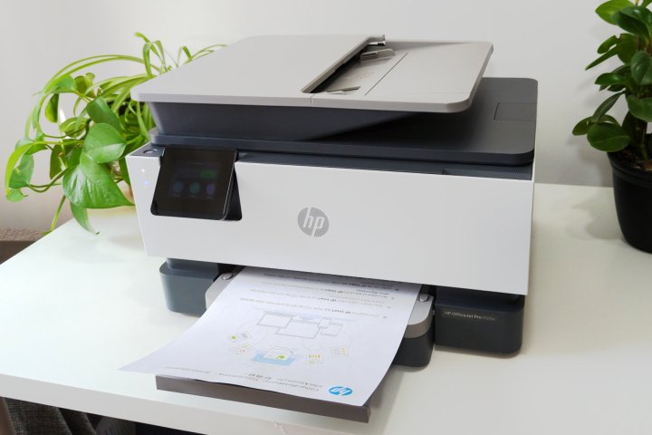La HP OfficeJet Pro 9125e repose sur un support blanc entouré de plantes.