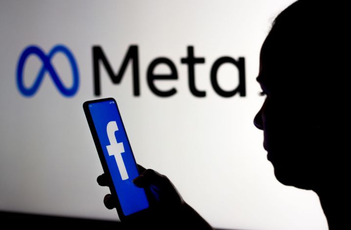 Le nouvel événement « Llamacon » de Meta : un rendez-vous incontournable pour l'IA open-source 1 Une personne silhouettée tient un smartphone affichant le logo de Facebook. Ils se tiennent devant un panneau affichant le logo de Meta.