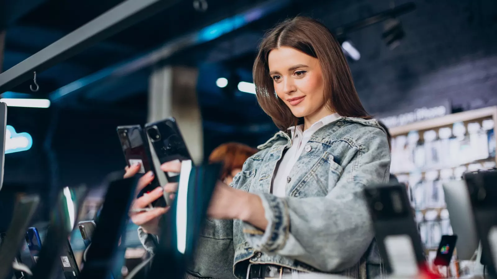 Les prix dévoilés des Redmi Note 15 reflètent le grand problème de l'industrie en vue de 2026 2 Femme regardant des téléphones dans un magasin.