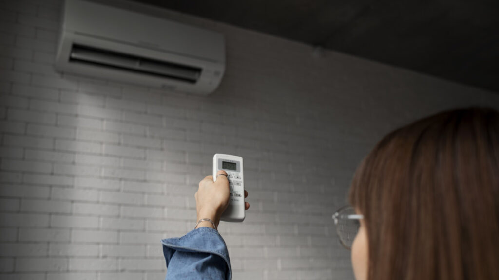 Dormir avec la climatisation allumée nuit-il véritablement à votre sommeil 4 Femme contrôlant un climatiseur avec une télécommande