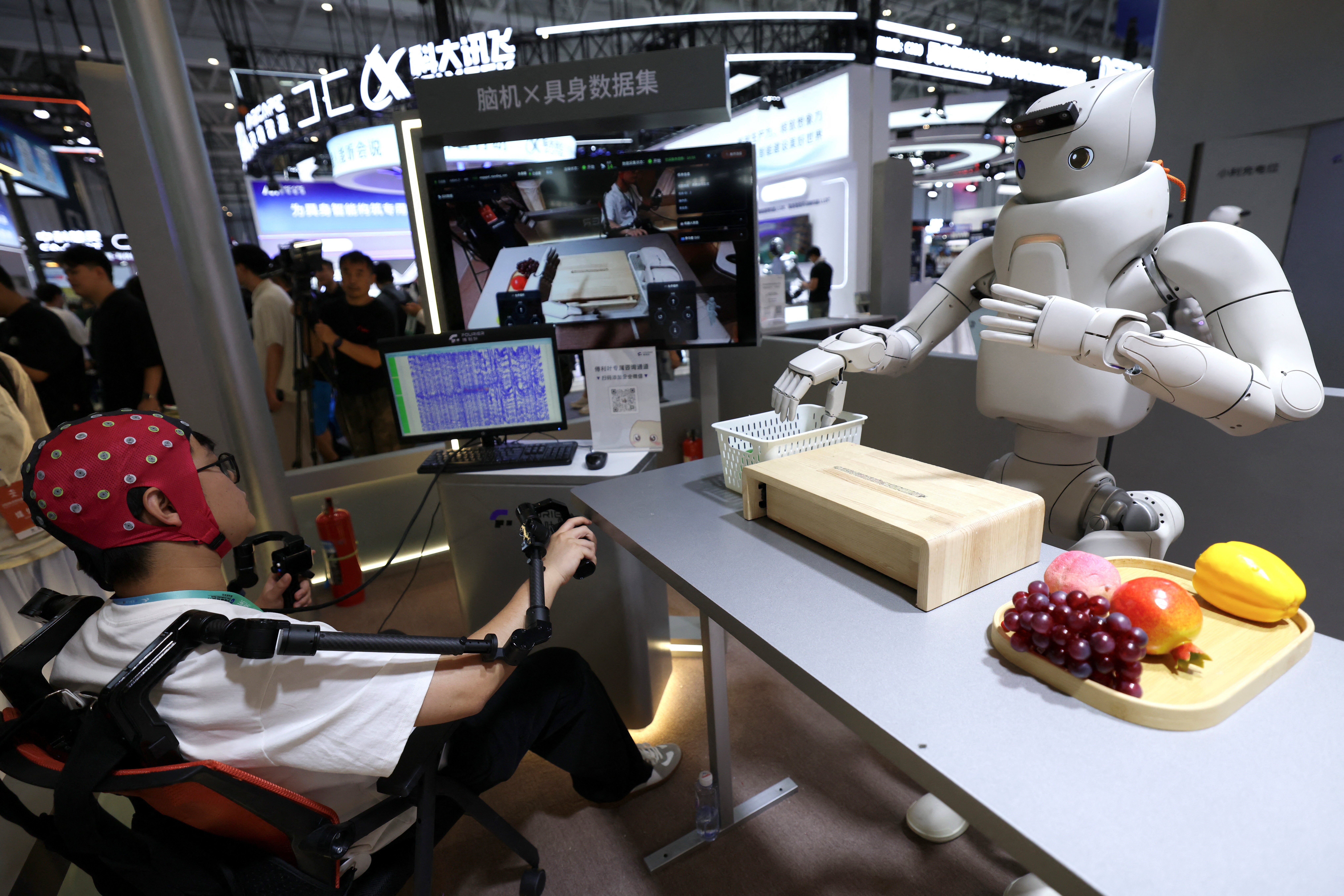 Un ingénieur porte un casque d’interface cerveau-ordinateur non invasif pour piloter un robot humanoïde, sur le stand Fourier Intelligence lors du World Robot Conference 2026.