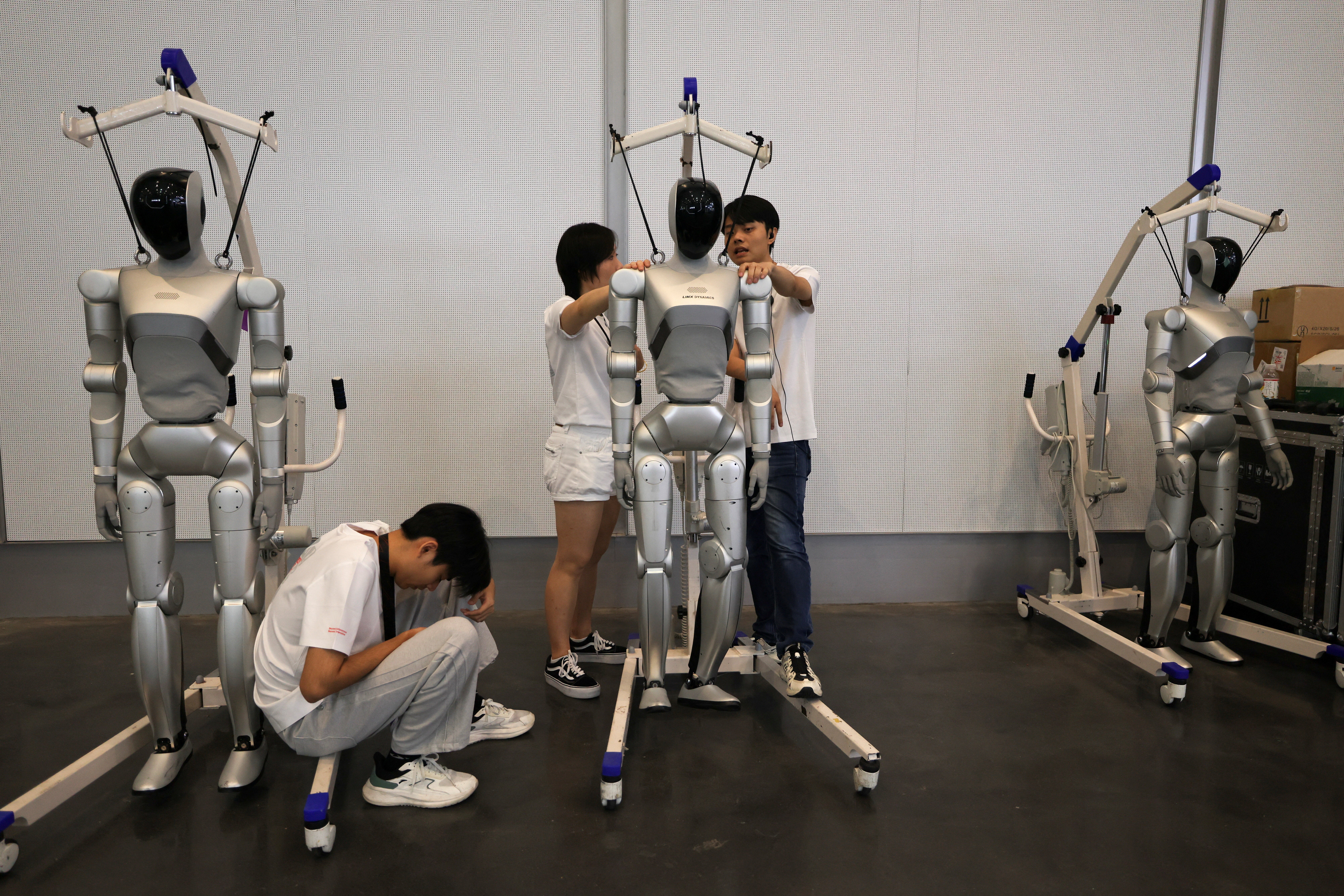 Des membres du personnel se tiennent près de robots humanoïdes de LimX Dynamics pendant le World Robot Conference 2026, à Pékin, Chine, le 19 août 2026.