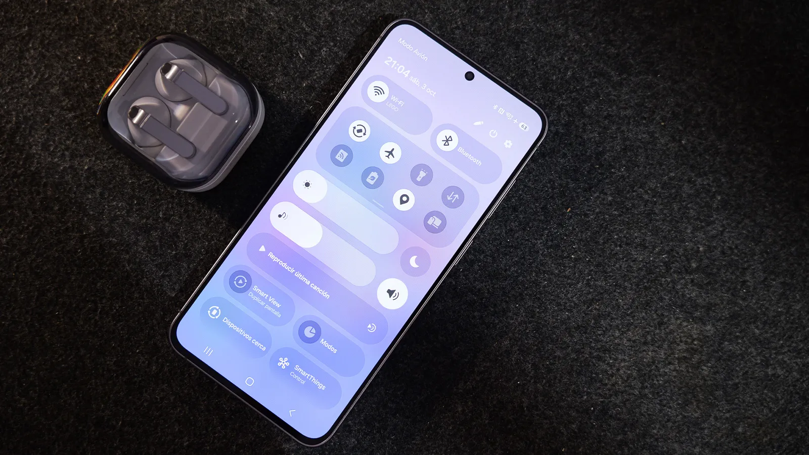 Mon expérience avec One UI 9 l'évolution dont les smartphones Samsung avaient besoin 3 Un téléphone mobile dont le panneau de réglages rapides de l'interface One UI est déployé, posé à côté d'écouteurs sans fil sur une surface sombre.