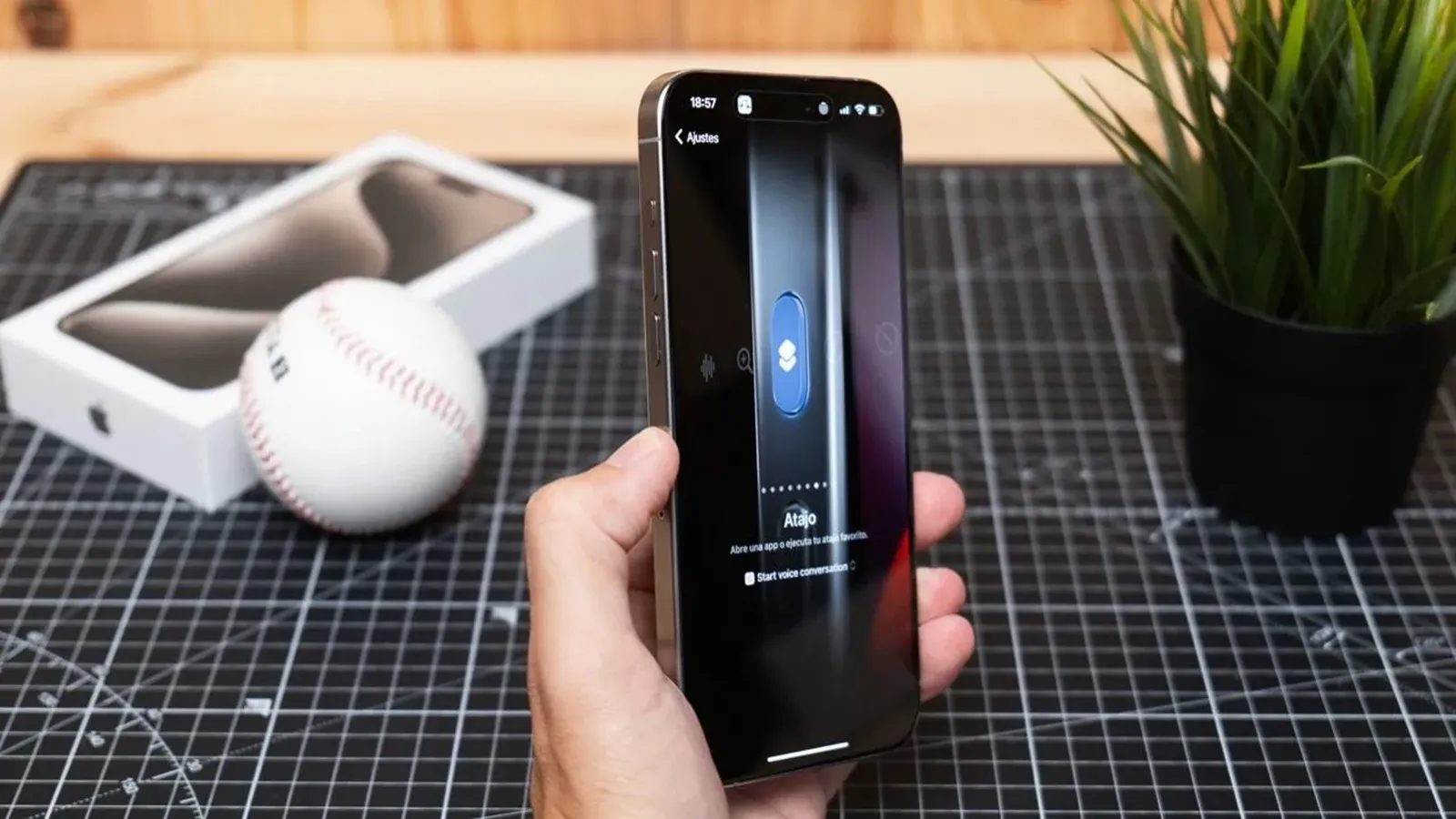 Fonctionnalités iOS 27 qui devraient devenir réalité sous Android 2 Gros plan sur une main tenant un iPhone 15 Pro Max avec le menu de configuration du bouton d'action affiché à l'écran, posé sur un plan de travail.